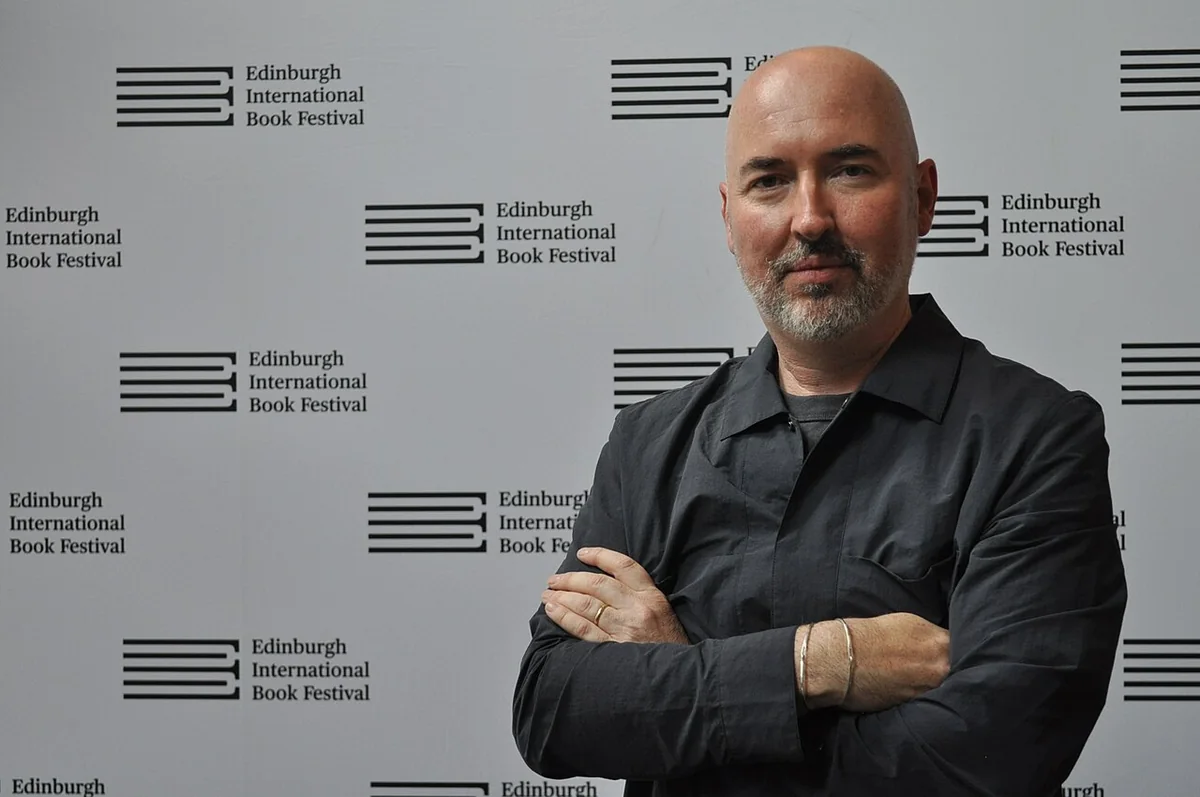 Douglas Stuart, arms folded, standing in front of an Edinburgh International Book Festival backdrop
