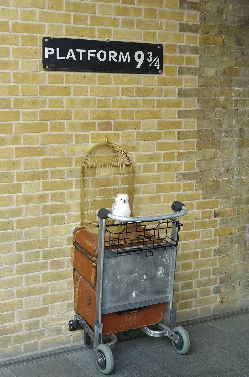 Platform 9 3/4 sign on a brick wall at King's Cross with a luggage trolley and owl cage set into the wall