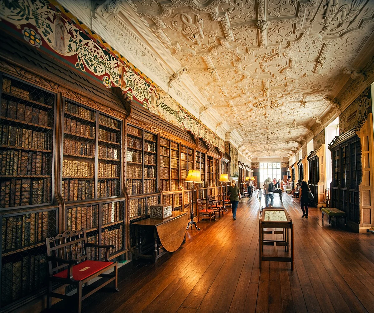 Long gallery library at Blickling Hall with leather-bound books in wire-fronted cases under a plaster ceiling