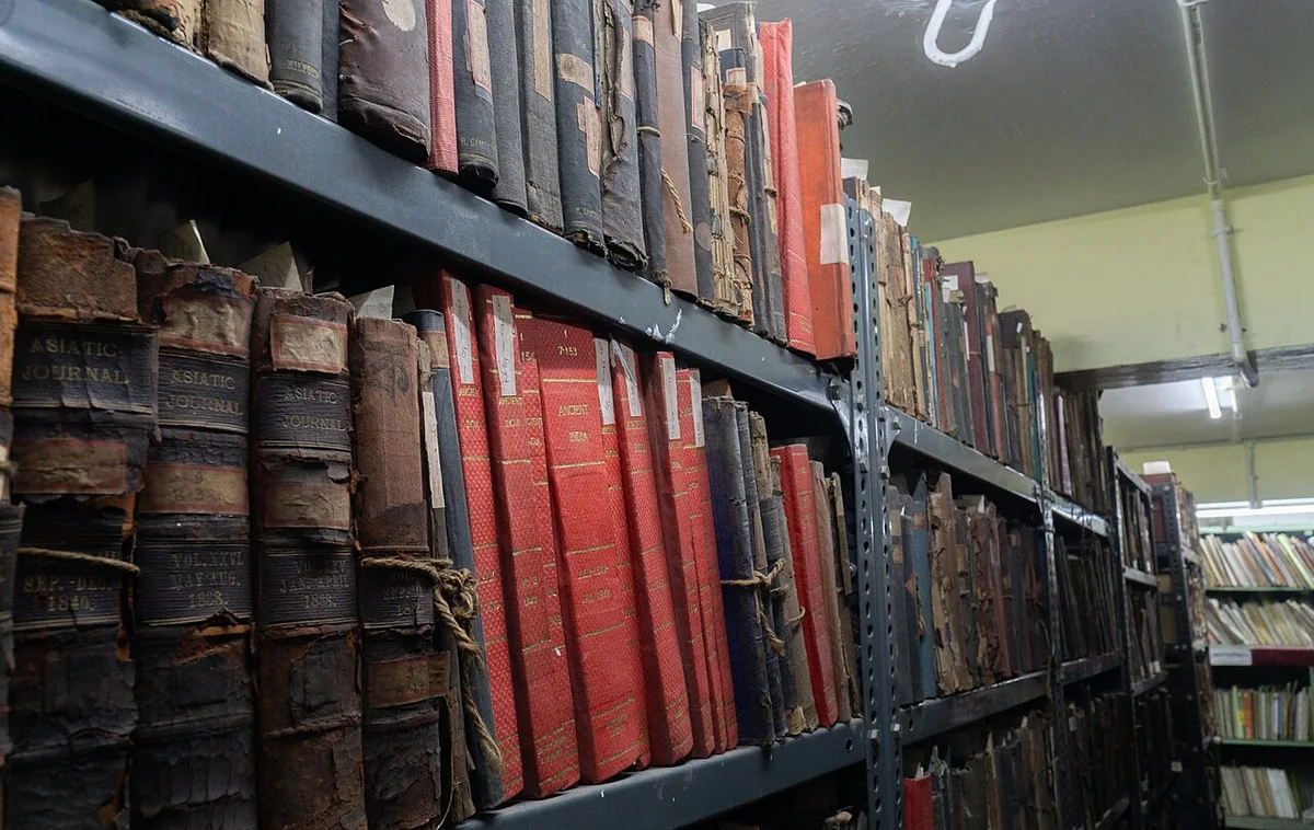 Close view of library shelves holding old volumes with cracked, flaking and string-tied leather spines