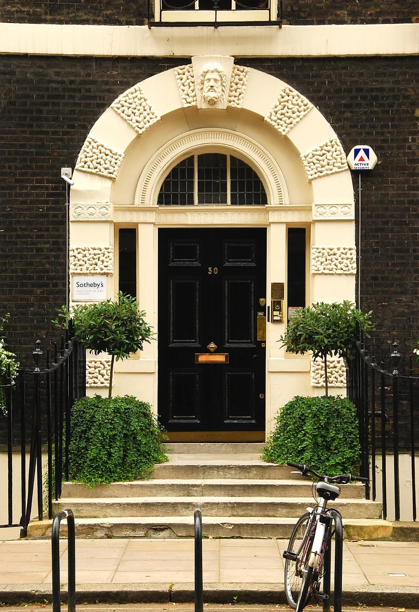 Black front door numbered 30 under a stone arch with a carved head, on a brick Georgian terrace