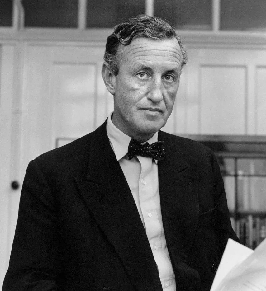 Black and white portrait of Ian Fleming in a dark jacket and polka-dot bow tie